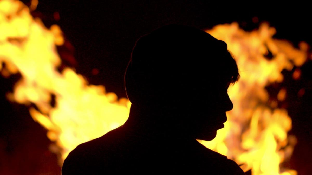 The sillouette of a young man's head and shoulders in profile, backlit by yellow-orange flames.