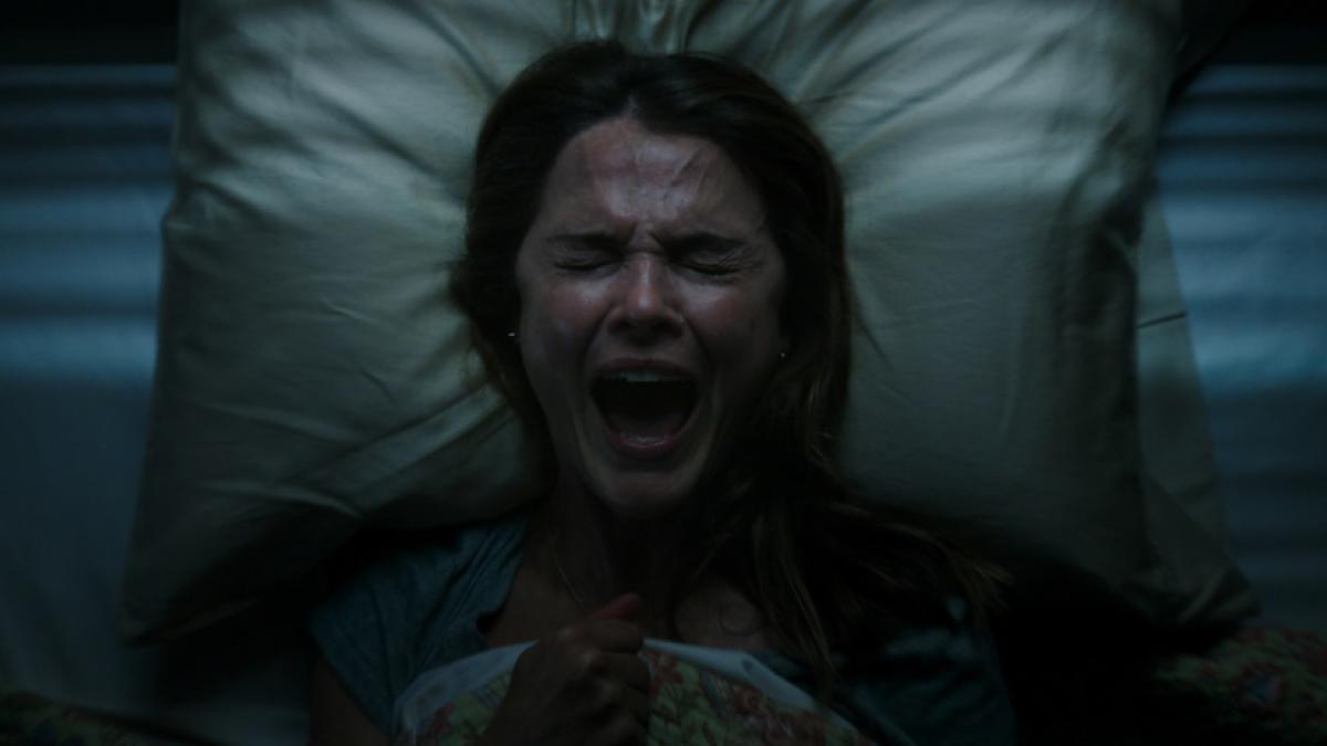 Close-up of a middle-aged woman lying in bed, screaming with her eyes shut tight.