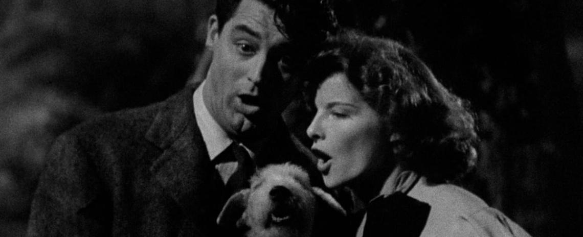A close-up of a man and woman holding a wire fox terrier while singing to/with it.